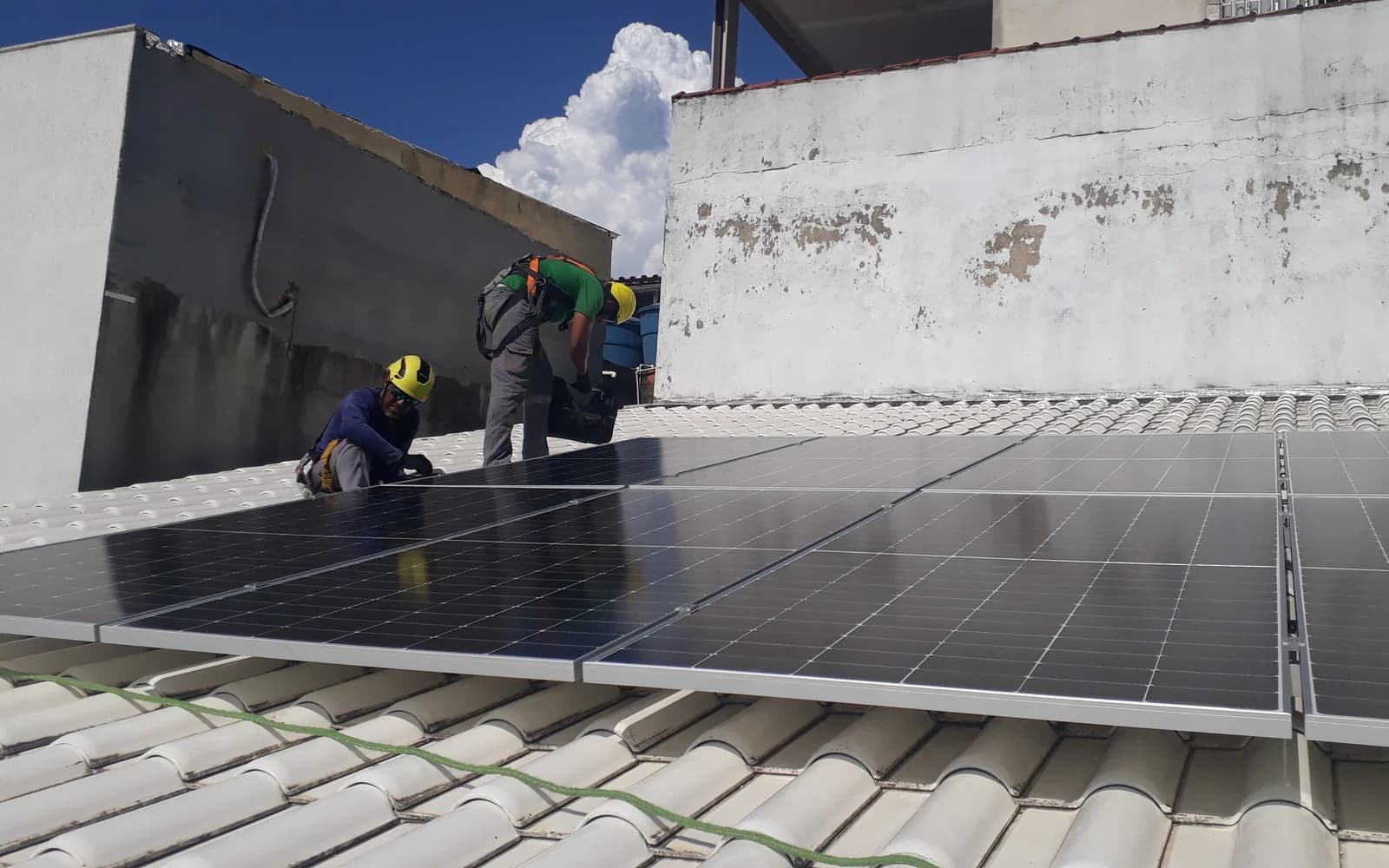 Técnicos com capacete e cinto de segurança montando módulos em telhado