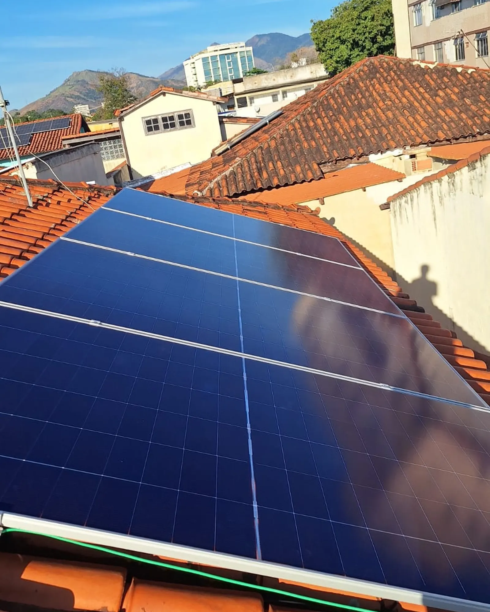 Módulos fotovoltaicos em telhado urbano no Rio de Janeiro, com a serra ao fundo